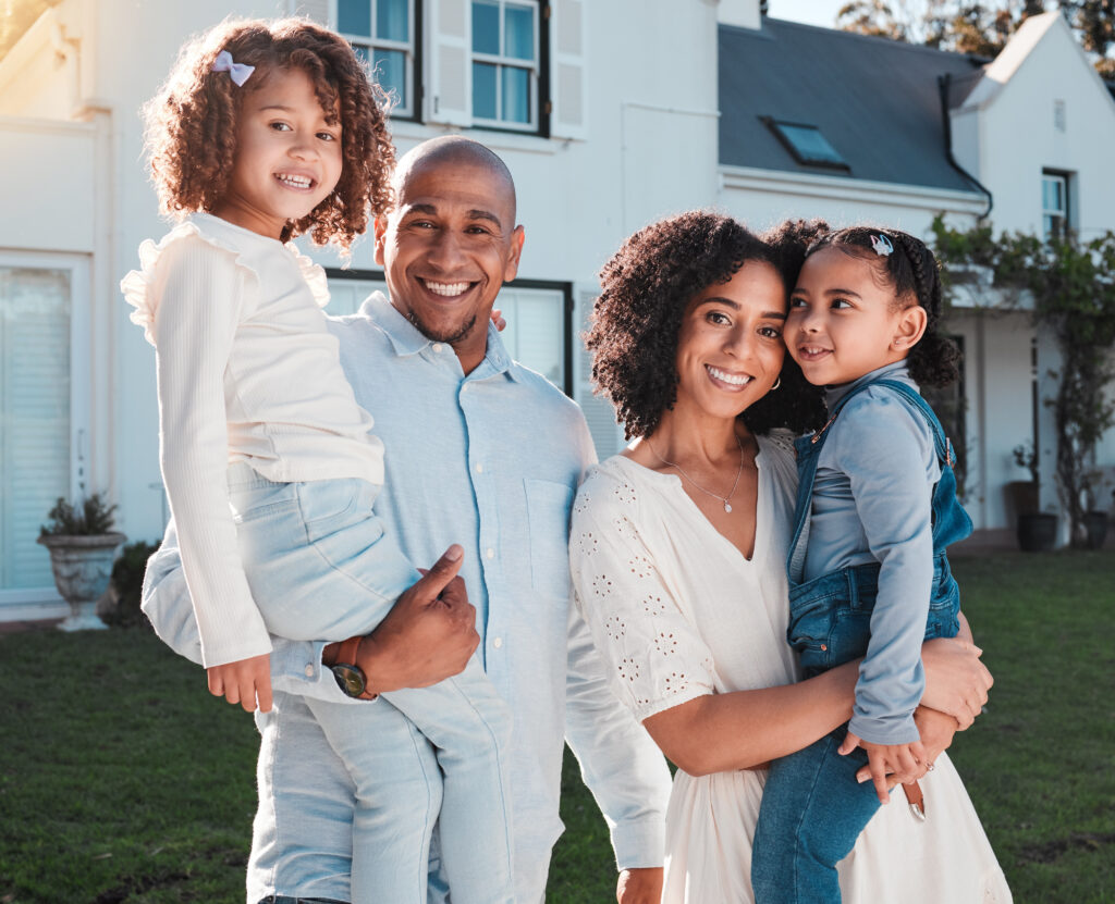 Happy family portrait outside their new home, parents holding children in backyard.