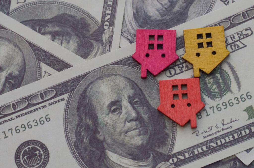 "Miniature house and colorful dice placed on US dollar bills symbolizing the downturn in property values and housing market uncertainty."