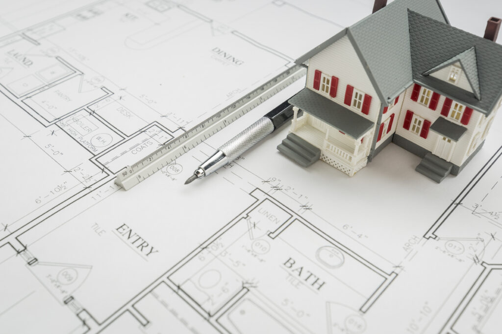 "Architectural model home with engineering pencil and ruler on blueprint plans"